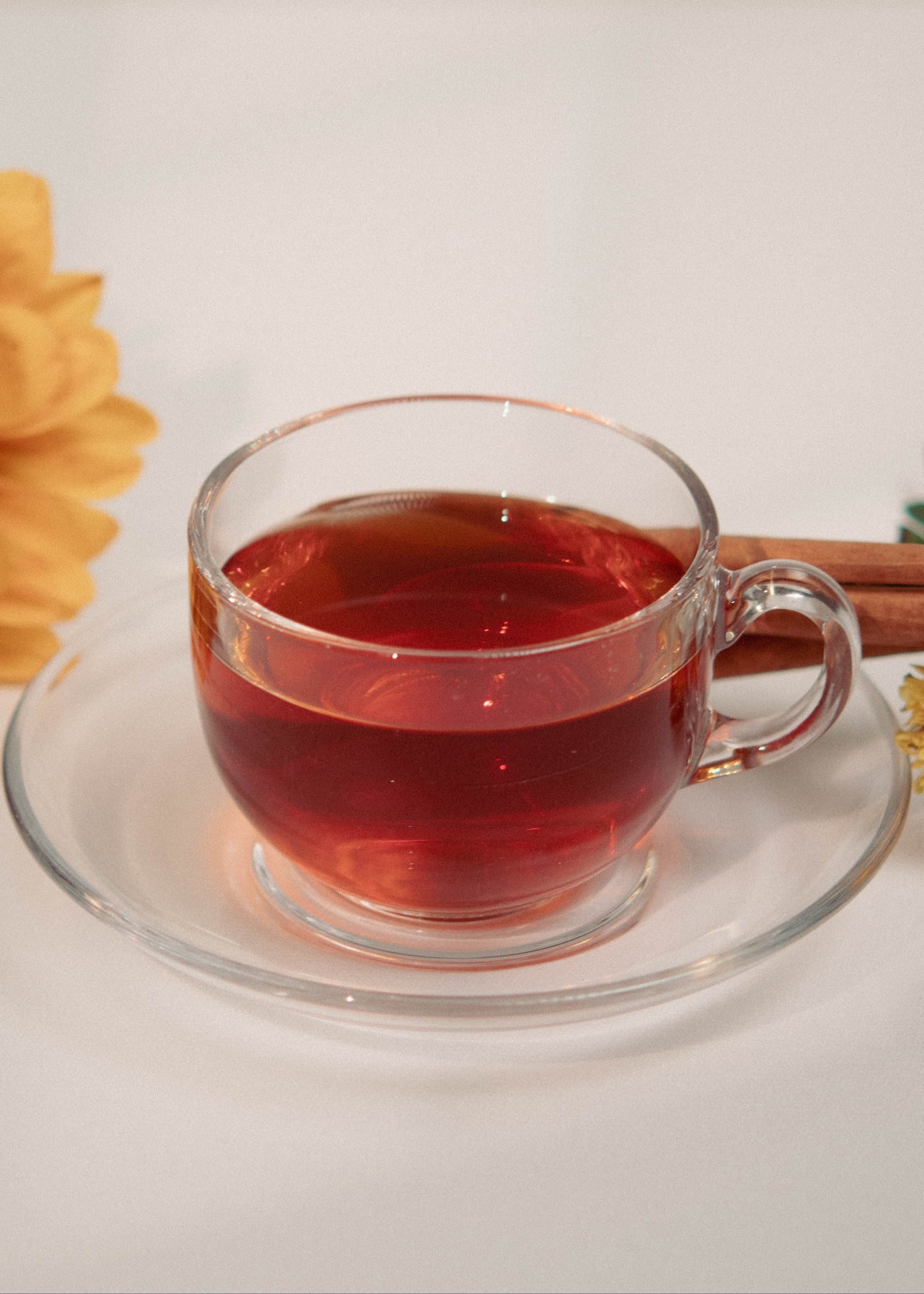 Clear glass mug with red liquid, sunflower, cinnamon stick, and small flowers on a white background