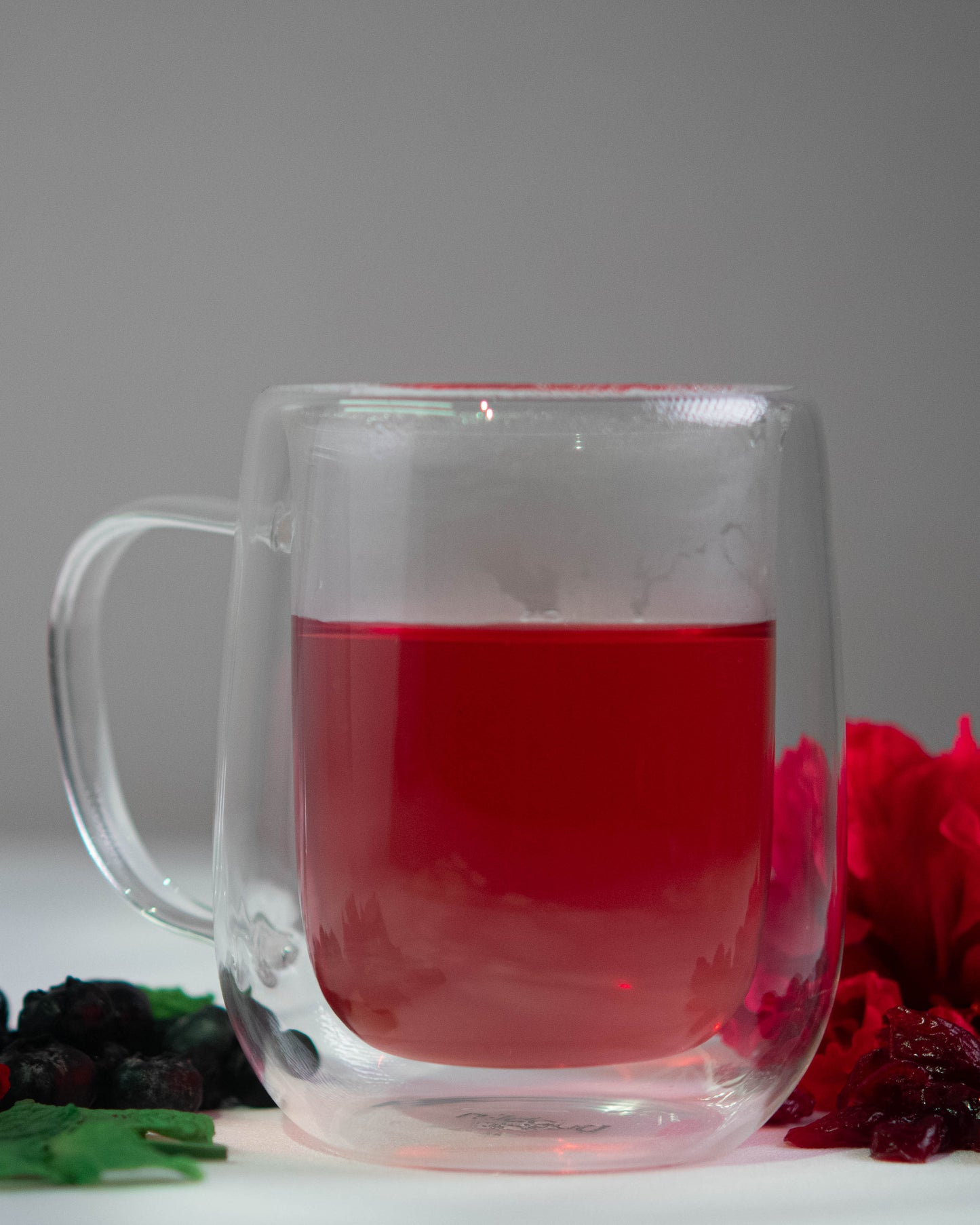 Clear glass mug with red liquid, surrounded by dried fruits and a red flower on a gray background