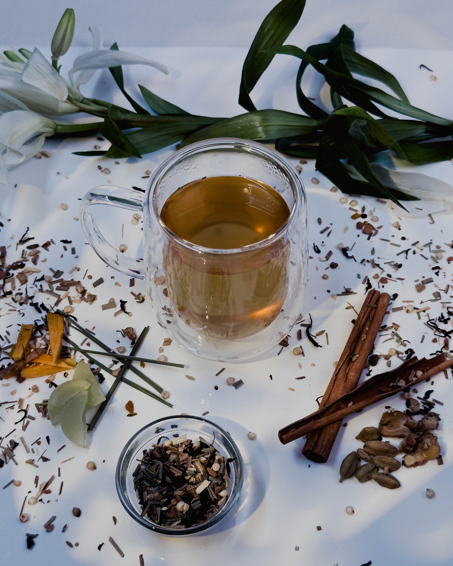 Tea cup with loose tea leaves, cinnamon sticks, and flowers on a white surface