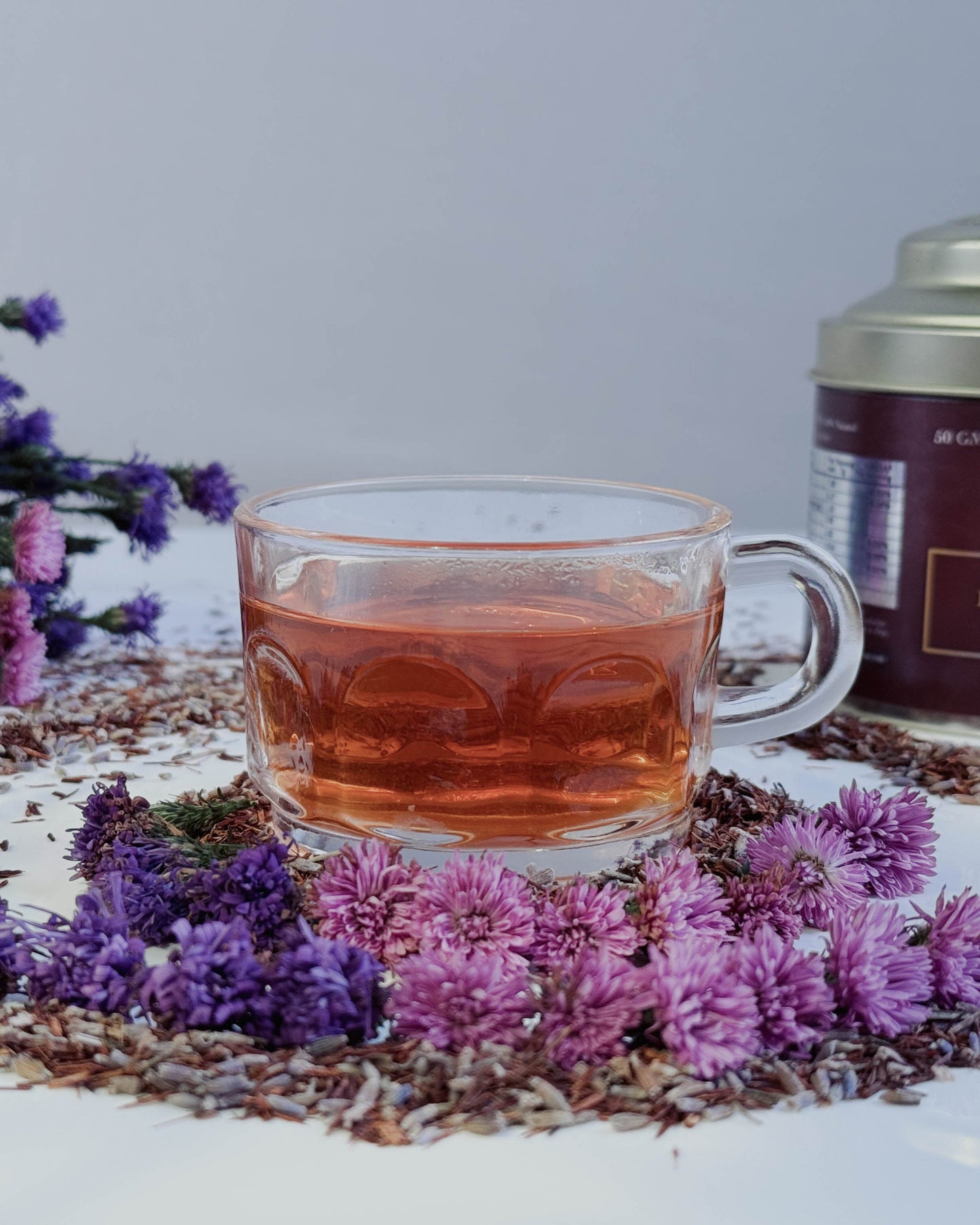Glass mug of tea with a canister labeled 'Ruby Dawn' on a decorative mat with flowers.