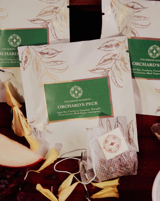Orchard's Peck tea packages with apples, cinnamon, and other ingredients on a wooden surface.