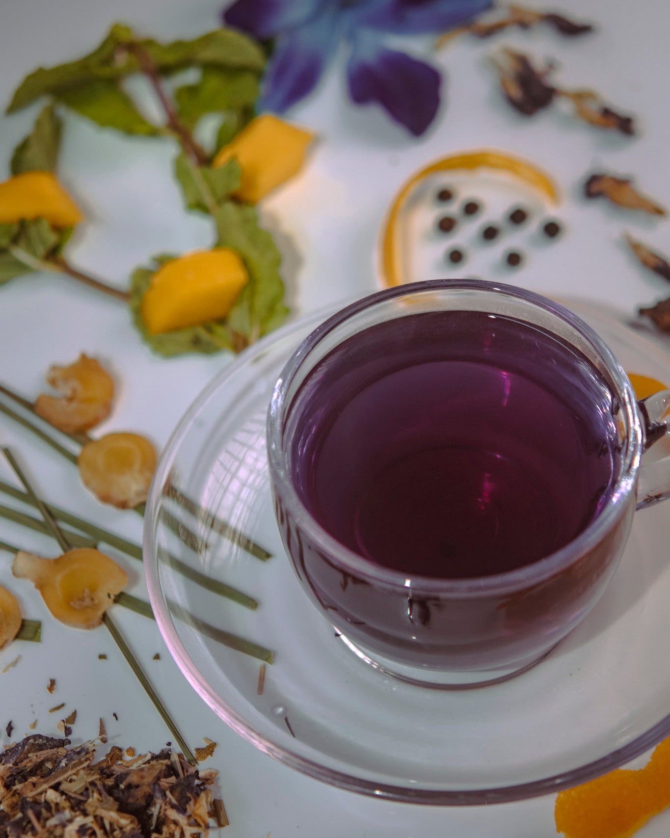Clear glass cup filled with purple liquid on a decorative saucer with floral and natural elements.