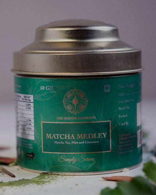 Matcha Medley tea canister with green label on a white surface with cinnamon sticks and flowers.