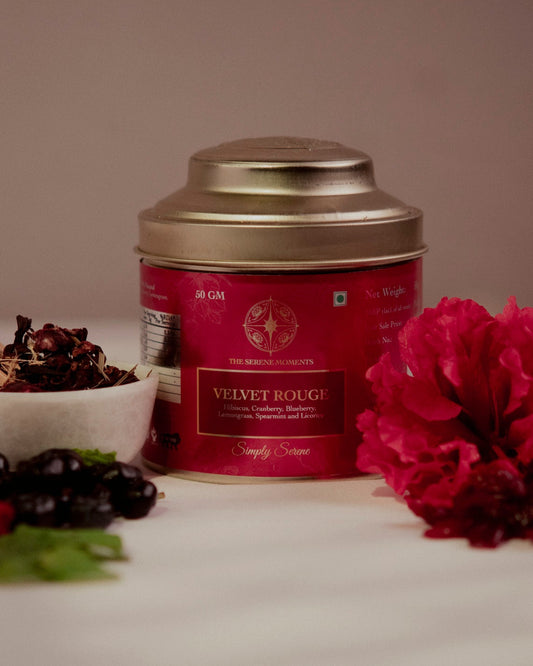 Red tea canister labeled 'Velvet Rouge' with a spoonful of tea and flowers on a neutral background