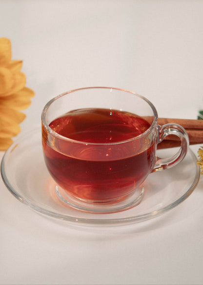 Clear glass mug with red liquid, sunflower, cinnamon stick, and small flowers on a white background