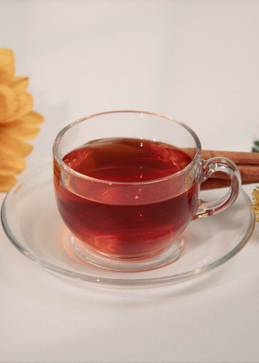 Clear glass mug with red liquid, sunflower, cinnamon stick, and small flowers on a white background