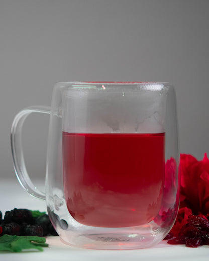Clear glass mug with red liquid, surrounded by dried fruits and a red flower on a gray background