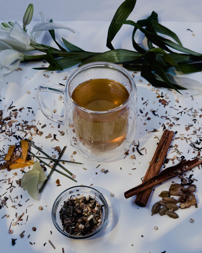 Tea cup with loose tea leaves, cinnamon sticks, and flowers on a white surface